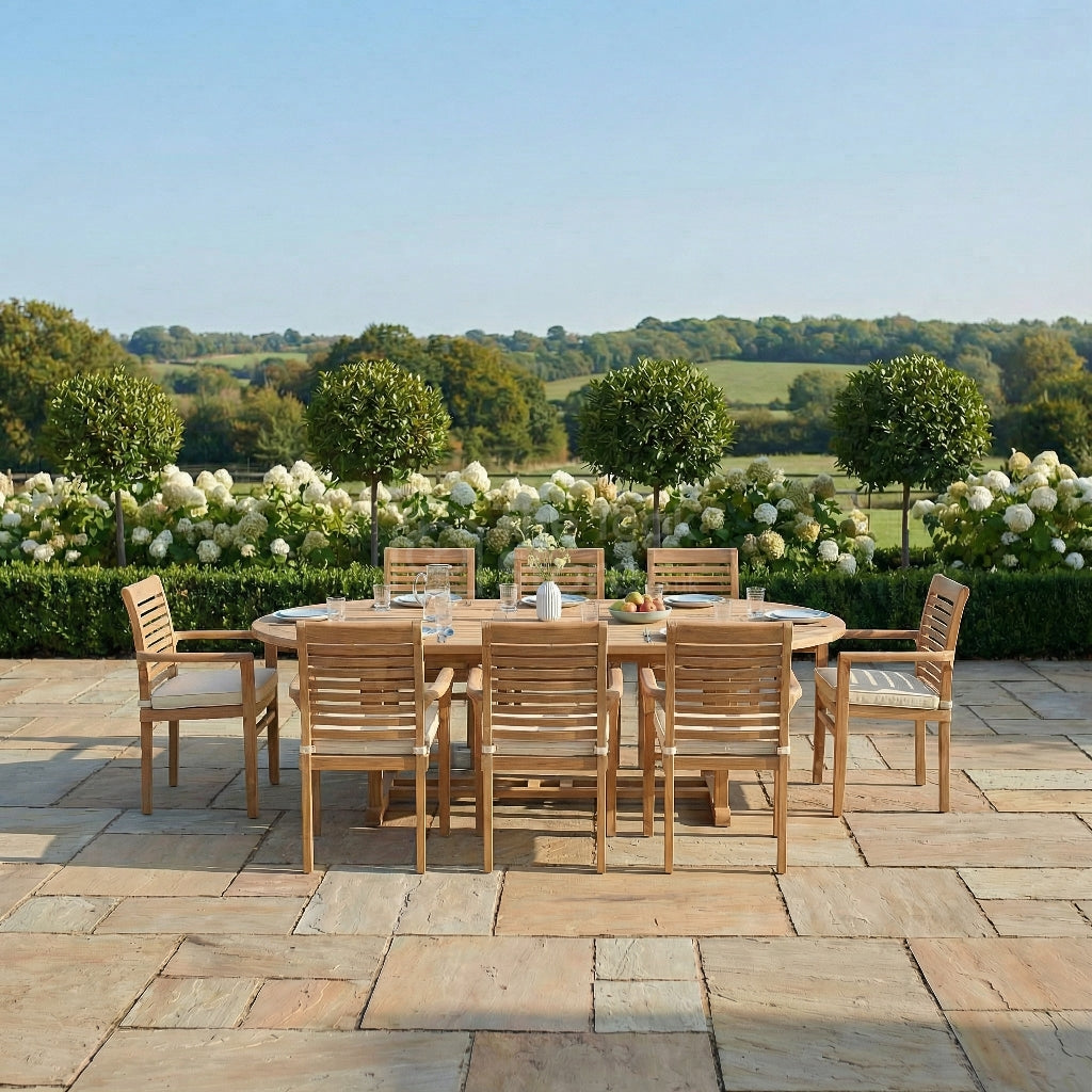 Outdoor dining set with wooden table and chairs on a stone patio, surrounded by greenery and flowers.