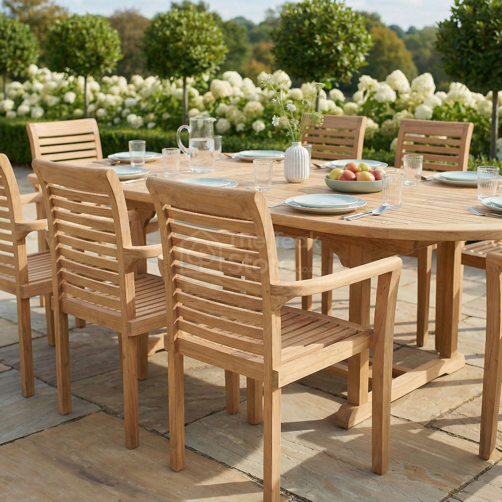 Wooden outdoor dining set with table and chairs on a stone patio, surrounded by greenery and flowers.