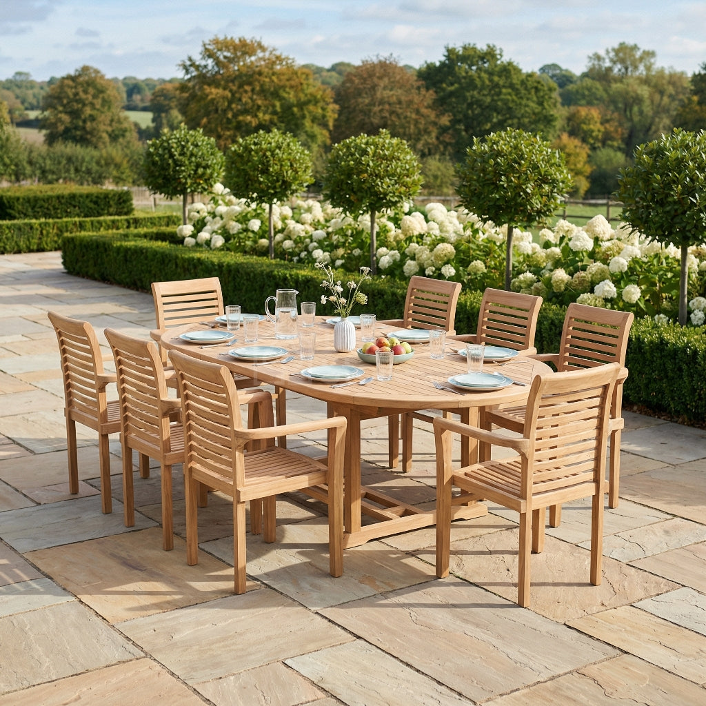 Wooden outdoor dining set with chairs on a stone patio, surrounded by greenery.